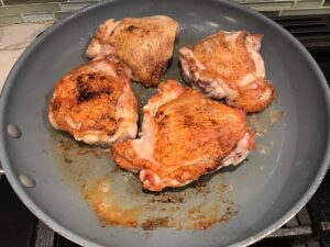 Seasoned chicken thighs cooking in a frying pan with the skin on for Crispy Sage Chicken, Butternut Squash, and Shallots.