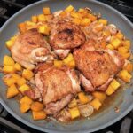 Seared chicken thighs, butternut squash cubes and shallots cooking in a frying pan for Butternut Squash and Chicken with Shallots.