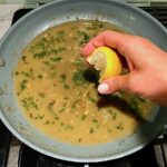 Hand squeezing a lemon over pan with sage and butter for Butternut Squash and Chicken with Shallots.
