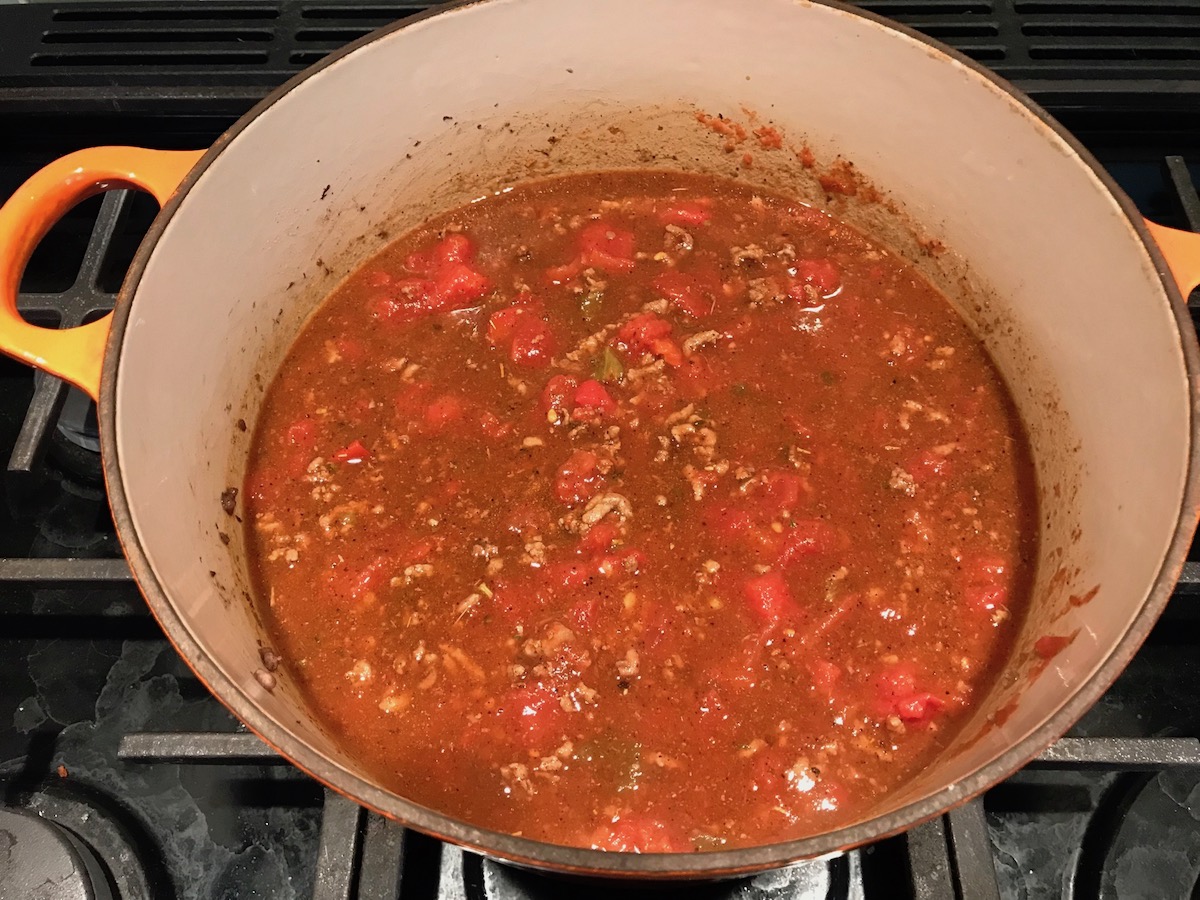 Tomatoes, chiles, and ground beef cooking in a pot for Southwestern Pasta with Ground Beef and Corn and breadcrumbs. The sauce is thick and hearty with ground beef, sweet corn kernels, chunky tomatoes, chipotle peppers in adobo, green chiles, parmesan cheese, and lots of smokey and spicy seasonings.