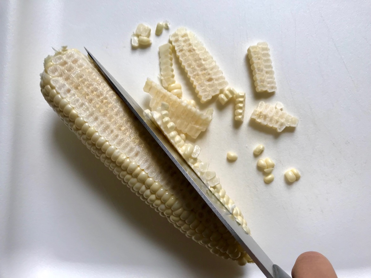 Knife cutting corn kernels off cob for Southwestern Pasta with Ground Beef and Corn and breadcrumbs. The sauce is thick and hearty with ground beef, sweet corn kernels, chunky tomatoes, chipotle peppers in adobo, green chiles, parmesan cheese, and lots of smokey and spicy seasonings.