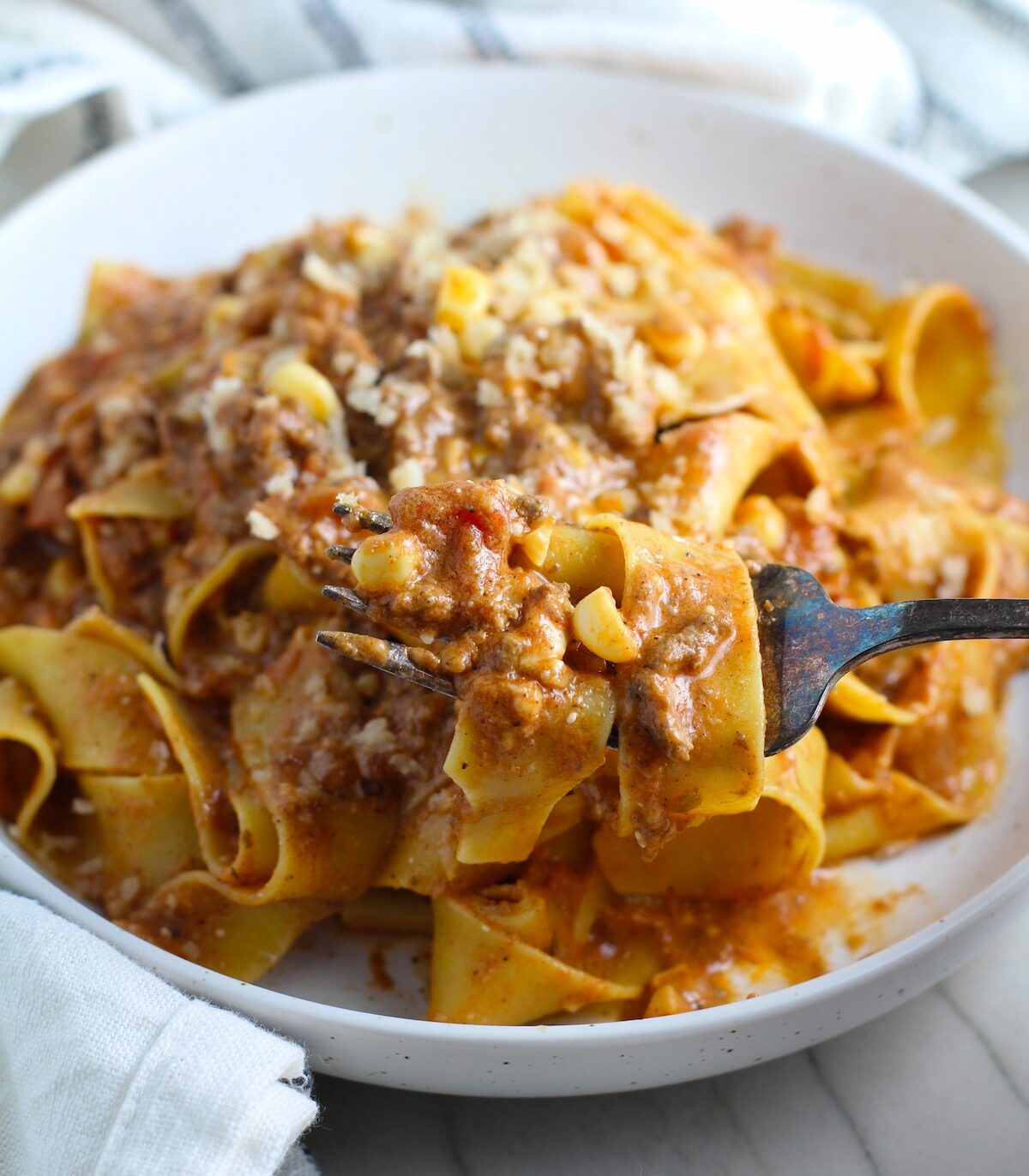Southwestern Pasta with Ground Beef and Corn and breadcrumbs on top on a plate with fork holding a bite. The sauce is thick and hearty with ground beef, sweet corn kernels, chunky tomatoes, chipotle peppers in adobo, green chiles, parmesan cheese, and lots of smokey and spicy seasonings.