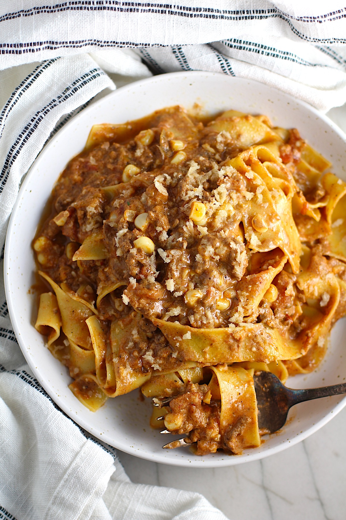 This photo show Southwestern Pasta with Ground Beef and Corn in a white bowl with a fork, ready to eat.