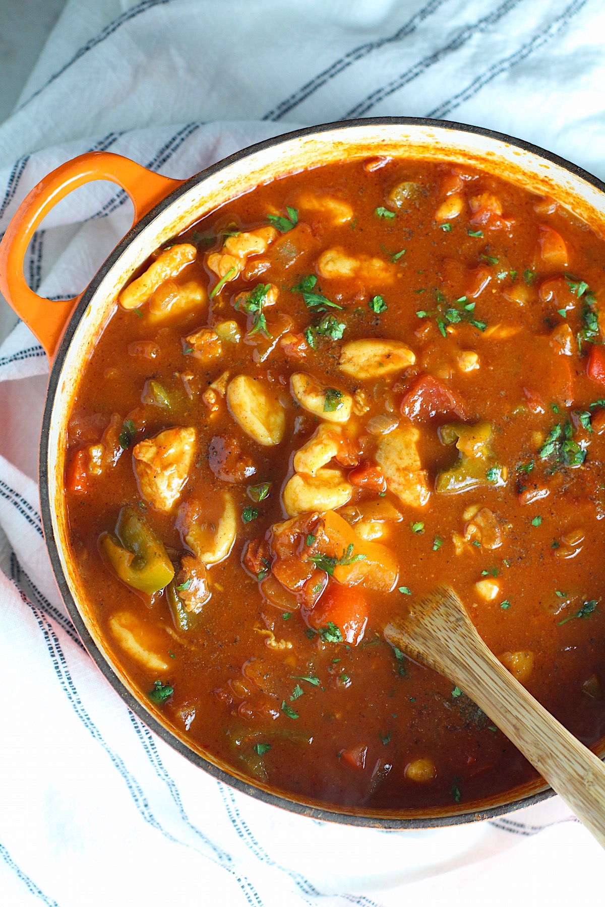 Chicken Goulash with quick homemade dumplings, red pepper, and parsley in a pot with a wood spoon.