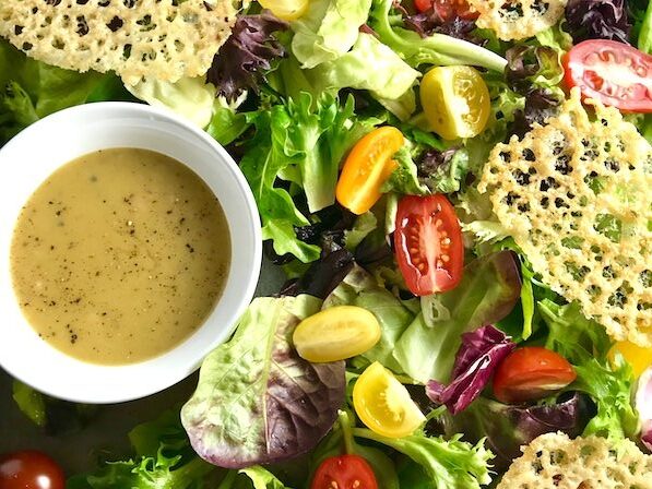 Salad on a platter with small bowl of vinaigrette and parmesan crips.