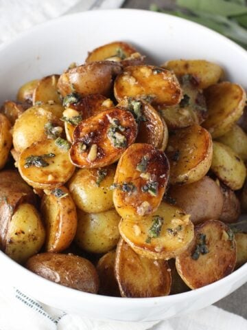 Crispy browned Sage Baby Potatoes with Garlic Butter in a bowl with garlic, sage butter glistening on top.