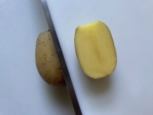 Knife cutting a creamer potato in half for Sage Butter Potatoes.
