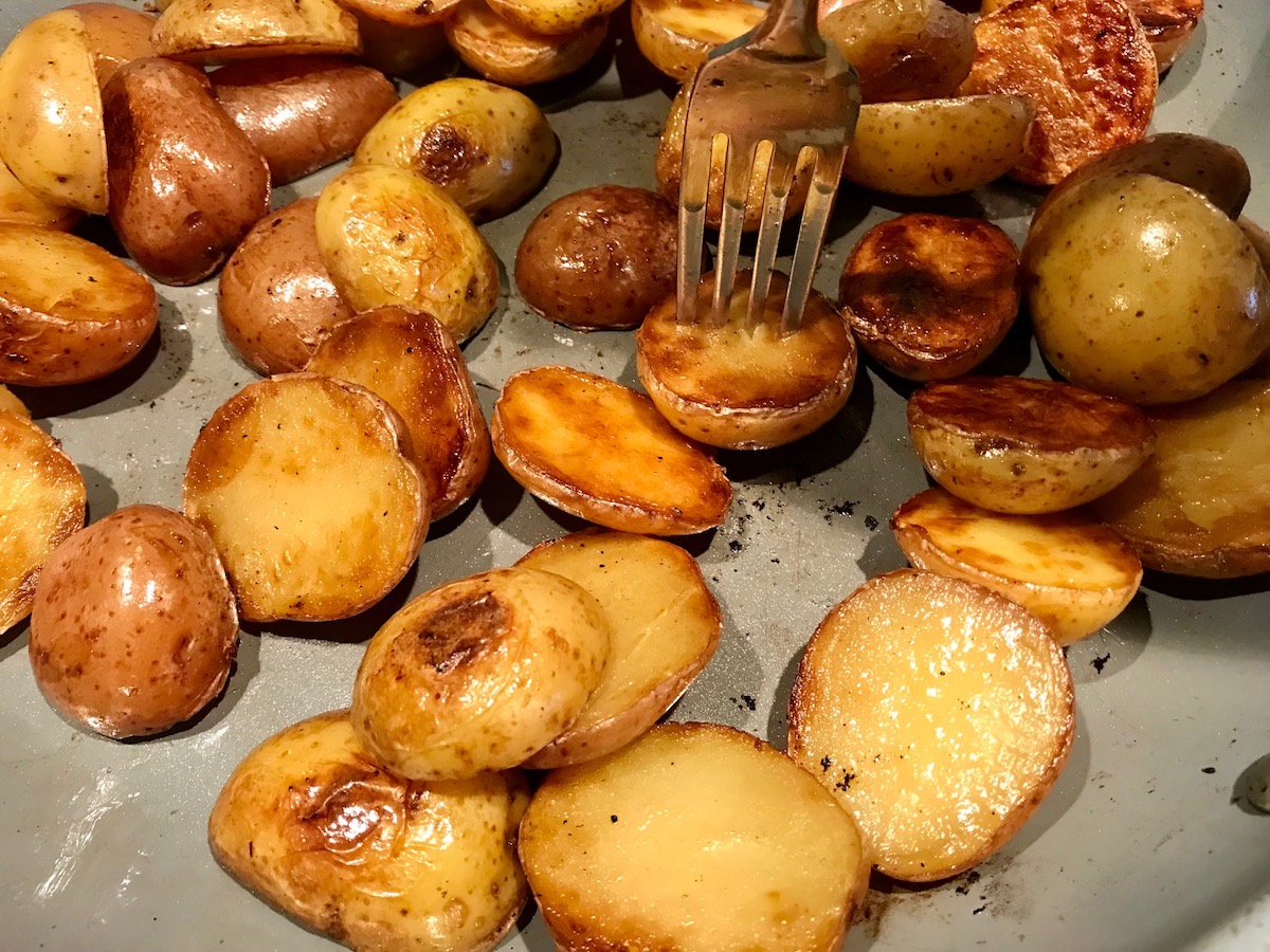 Browned and crispy halved red and gold creamer potatoes in a skillet with a fork in one potato for Sage Butter Potatoes.