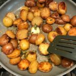 Browned and crispy halved red and gold creamer potatoes in a skillet with garlic, sage, and melted butter for Sage Butter Potatoes.