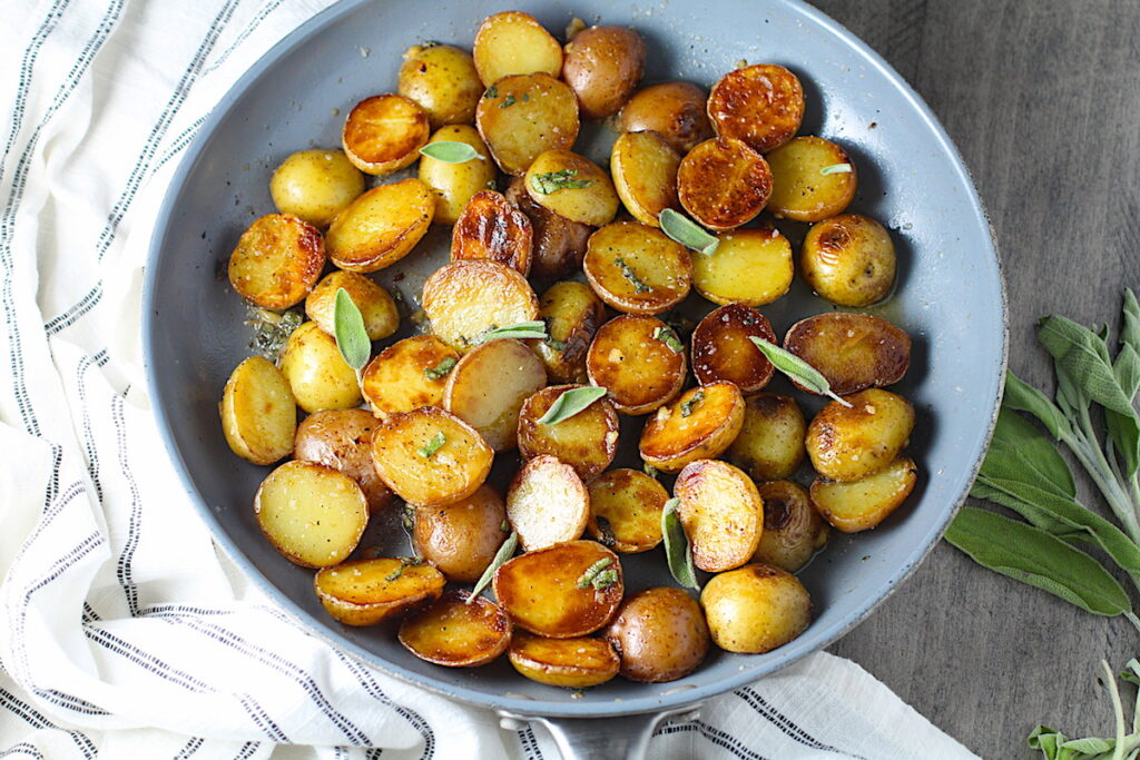 Crispy browned Sage Butter Potatoes in a skillet with garlic, sage butter glistening on top.
