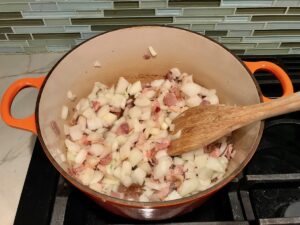 Bacon and diced onions in pot cooking with wooden spoon for Chicken Goulash with quick homemade dumplings.