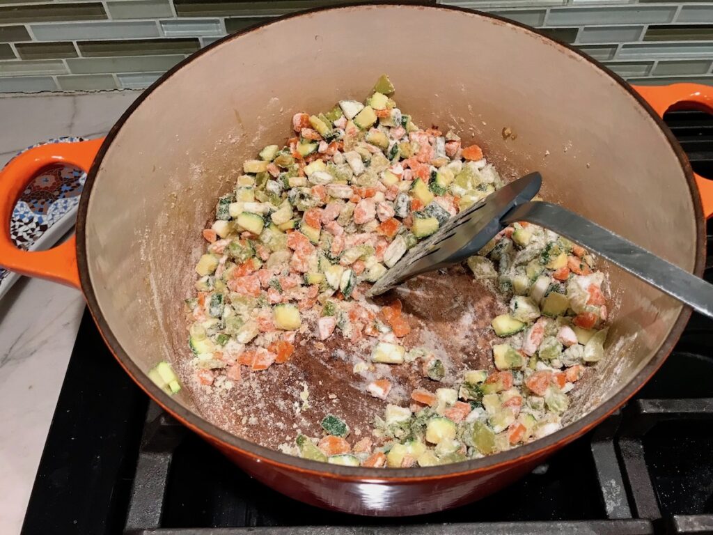 Spatula mixing flour into carrots, celery, and zucchini cooking in pot for Puff Pastry Turkey Pot Pie. It's an easy dinner recipe to use leftover turkey from the holidays and ingredients you can have on hand! The vegetables and sauce come together so easily and store-bought puff pastry is a time saver.