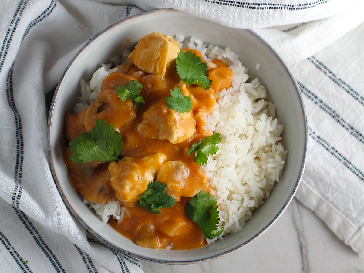 Chicken Stroganoff Brazilian Style in a bowl with a tomato based sauce, cream, mushrooms and cilantro leaves on top all over rice.
