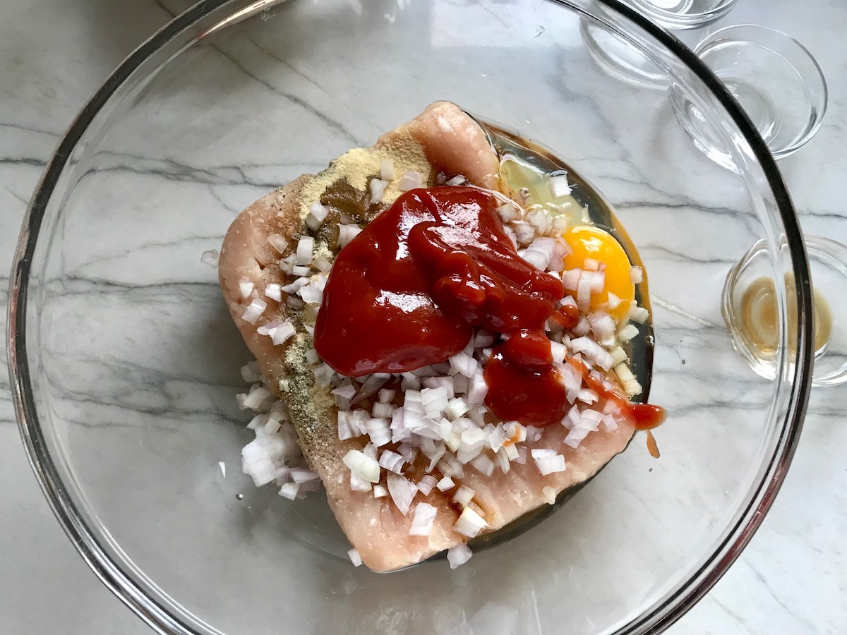 Raw ground chicken, diced onion, egg, and ketchup in a bowl for Ground Chicken Meatloaf. It's a perfect family dinner main dish!  10 minutes to prep and 45 minutes to bake.
