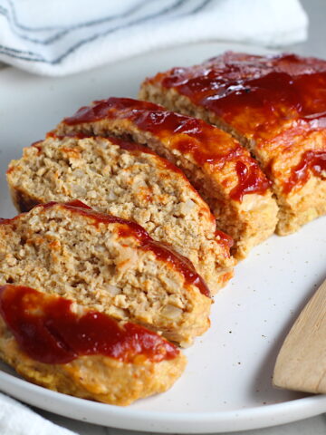 Ground Chicken Meatloaf with ketchup on top sliced and fanned out on plate with spatula on side and towel next plate. It's a perfect family dinner main dish! 10 minutes to prep and 45 minutes to bake.