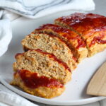 Ground Chicken Meatloaf with ketchup on top sliced and fanned out on plate with spatula on side and towel next plate. It's a perfect family dinner main dish!  10 minutes to prep and 45 minutes to bake.