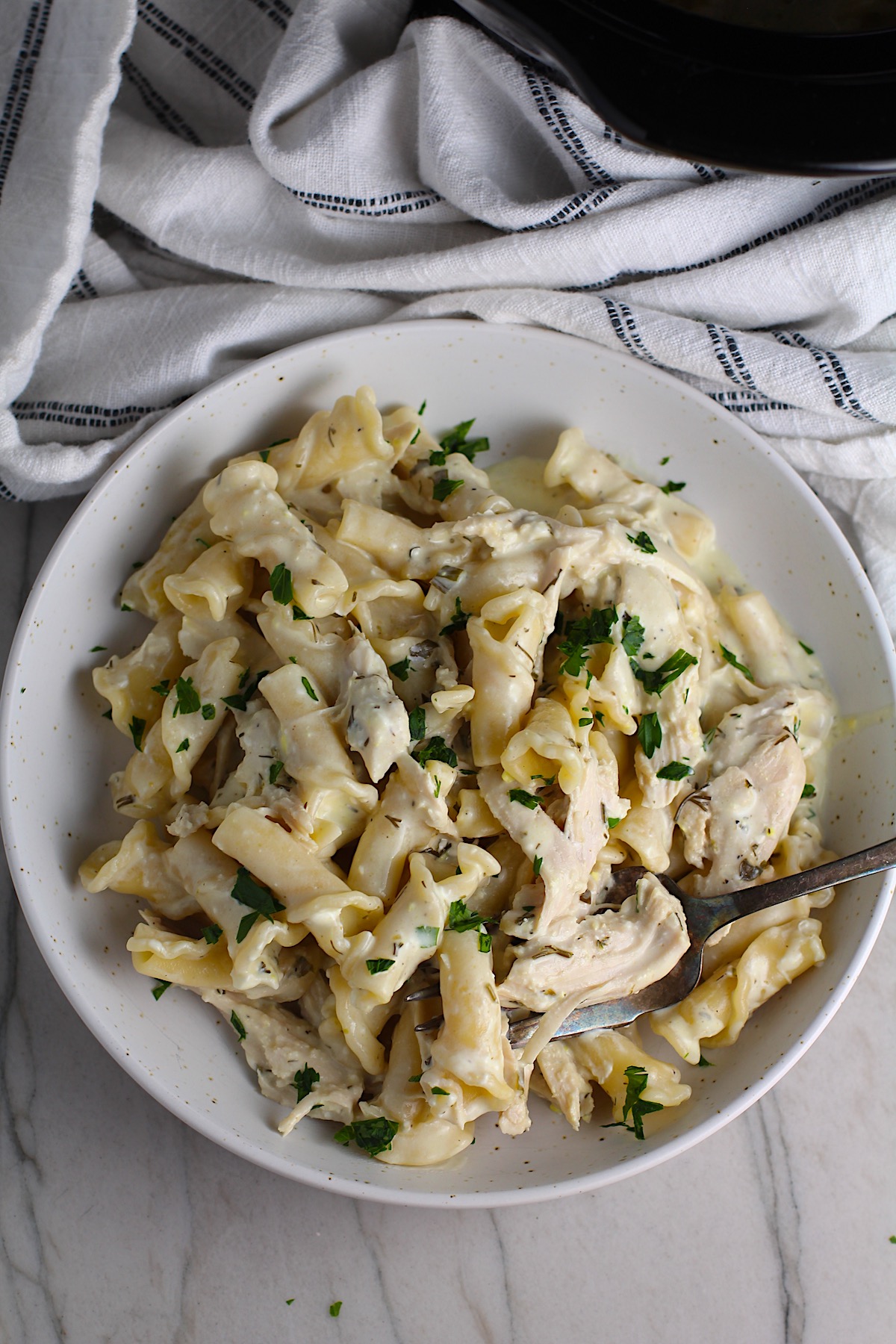 Ranch Chicken Crock Pot Pasta on a plate with fork and towel next it on counter. It uses fresh dill, parsley, and scallions is creamy, tangy, and utterly delicious!  It's also so easy to make, so it's a great weeknight dinner.