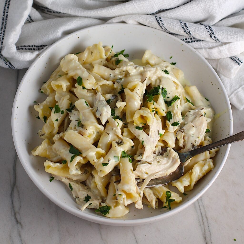 Ranch Chicken Crock Pot Pasta on a plate with fork and towel next it on counter. It uses fresh dill, parsley, and scallions is creamy, tangy, and utterly delicious!  It's also so easy to make, so it's a great weeknight dinner.
