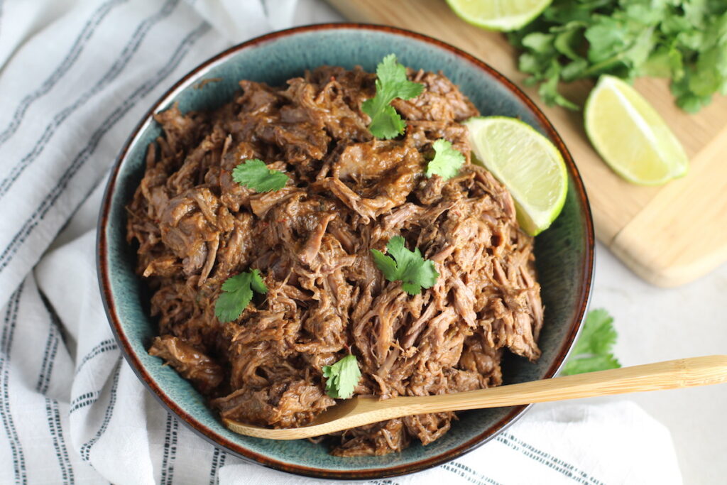 Cooked shredded beef in a bowl with cilantro garnish for post 'Can you freeze pulled pork'.