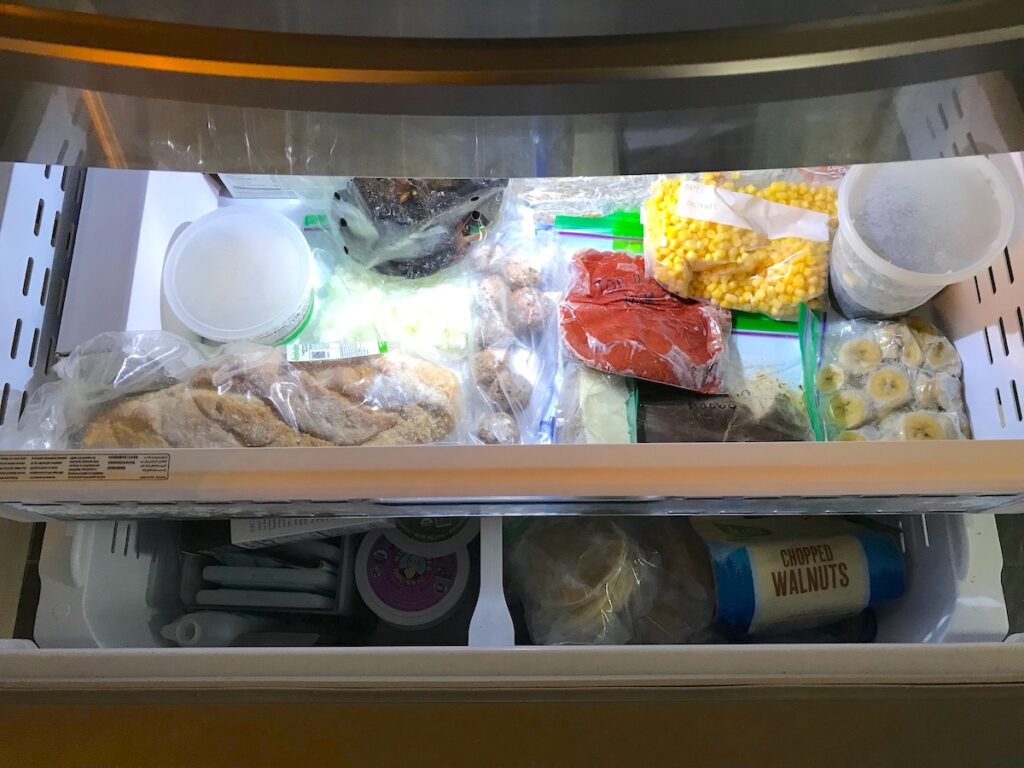 Pull-out drawer freezer filled with frozen veggies, bread, sauce, bananas, corn, and more for post 'Can you freeze pulled pork'.