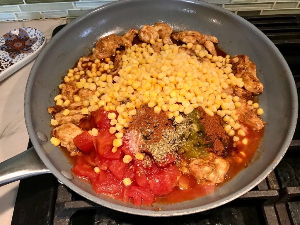 Skillet with Mexican Marinated Chicken, tomatoes, green chiles, corn, and seasonings.
