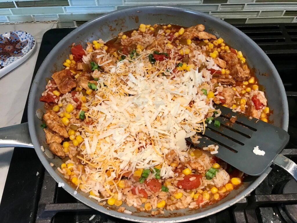 Shredded cheese added to Mexican Marinated Chicken and Rice skillet on stove.