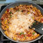 Shredded cheese added to Mexican Marinated Chicken and Rice skillet on stove.