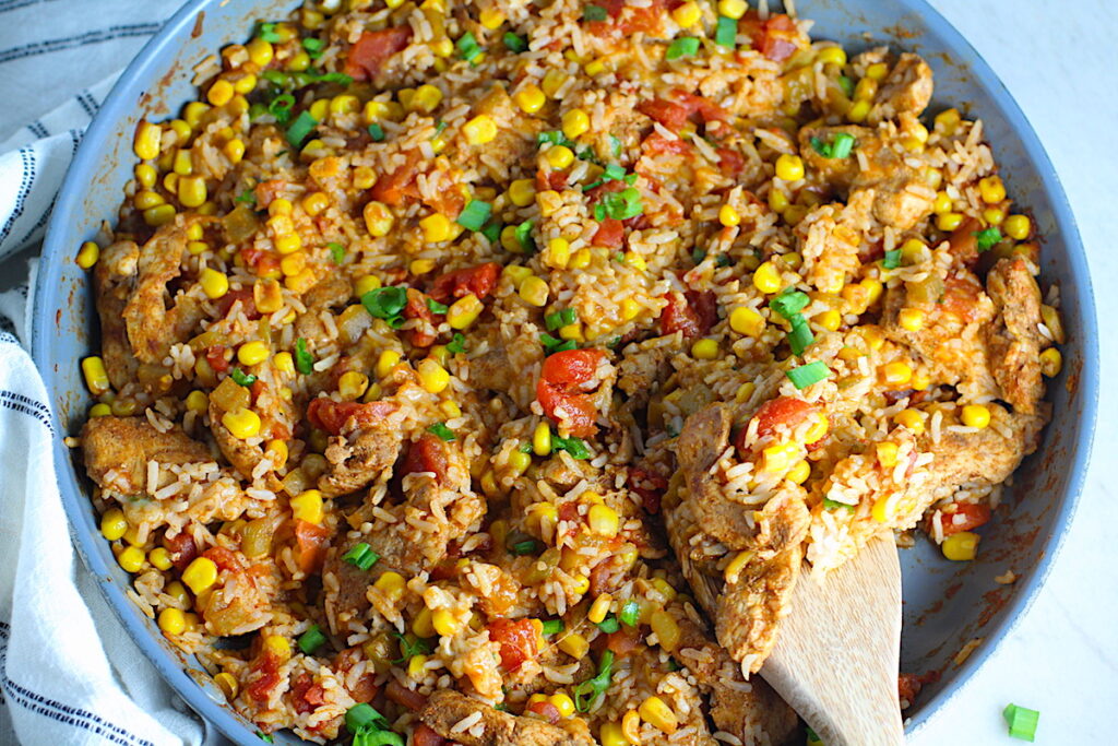 Mexican Marinated Chicken and Rice Skillet with tomatoes, corn, and scallions. Spatula scooping inside the skillet.