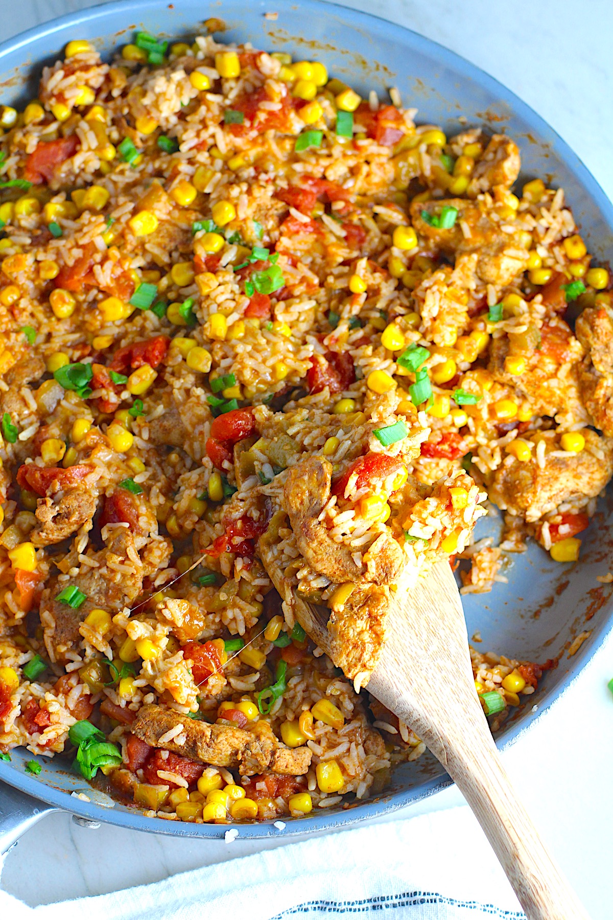 Mexican Marinated Chicken and Rice Skillet with tomatoes, corn, and scallions. Spatula scooping inside the skillet.