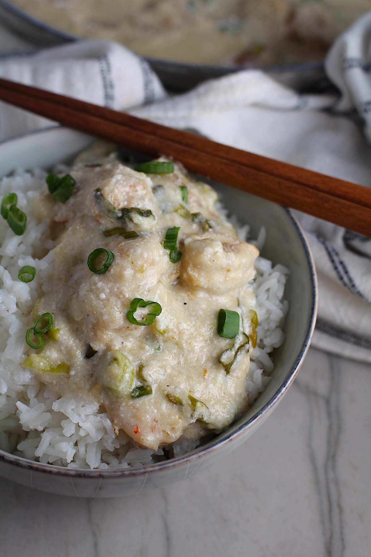 Creamy Chinese Coconut Shrimp Recipe over rice in bowl garnished with scallions and chopsticks on edge of bowl. It's filled with flavor from garlic, ginger, coconut, and more. Done in under 30 minutes, it's perfect for busy nights!