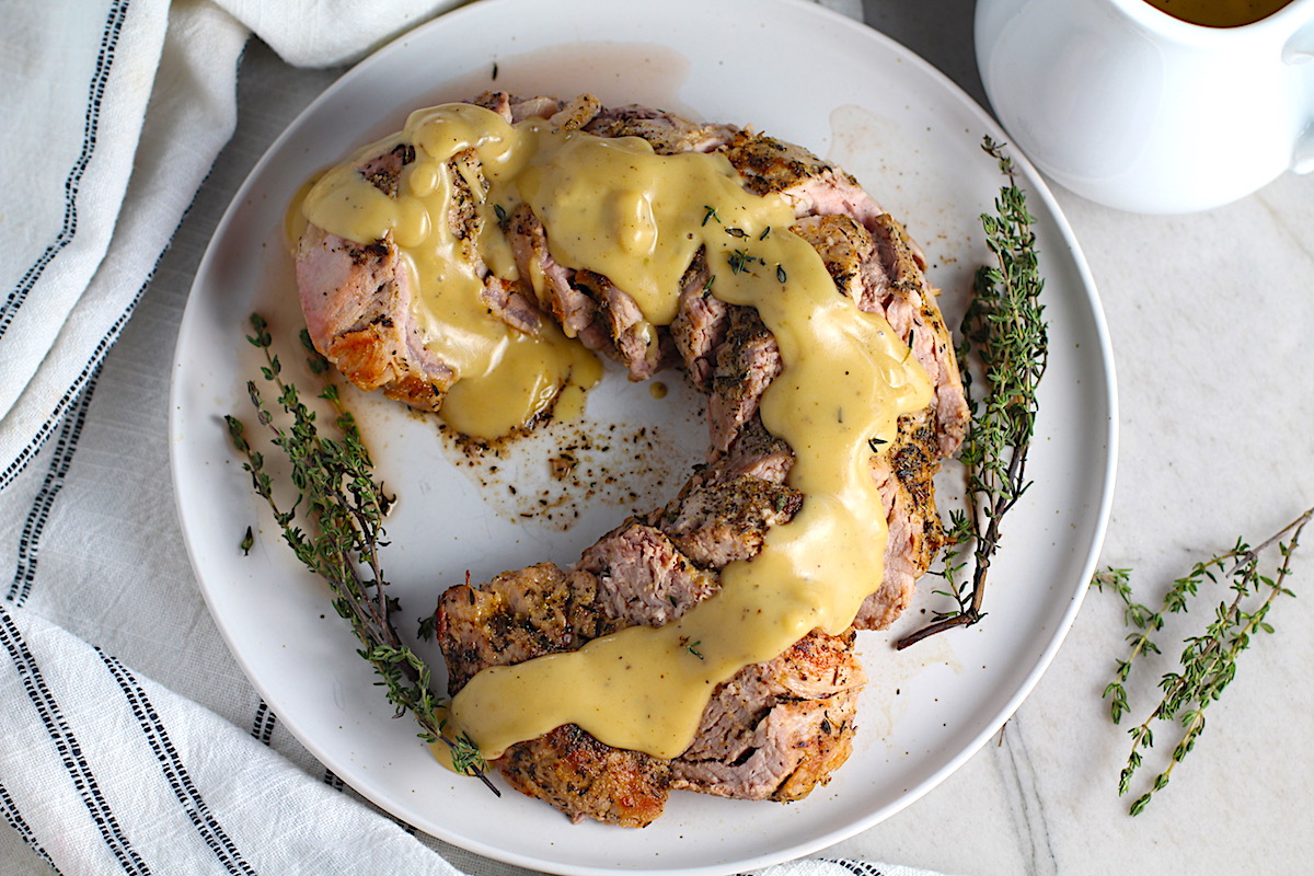 Roast Pork Gravy Recipe on sliced pork tenderloin on a platter with fresh thyme. It's thick, creamy, and full of flavor from garlic, thyme, and pork drippings.
