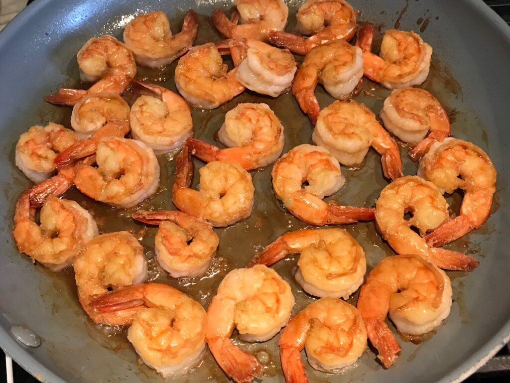 Shrimp cooking in a pan on stove for Shrimp Mei Fun Recipe, Singapore Noodles. It's an easy stir fry to make at home and tastes so much better than take out! With carrots, bean sprouts, curry powder, sesame oil, and more it's is a 30 minute weeknight dinner.
