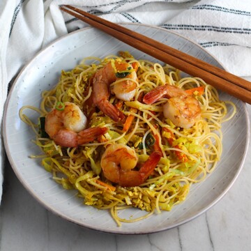 Shrimp Mei Fun Recipe, Singapore Noodles, on a plate with brown wood chop sticks on counter with napkin. It's an easy stir fry to make at home and tastes so much better than take out! With carrots, bean sprouts, curry powder, sesame oil, and more it's is a 30 minute weeknight dinner.