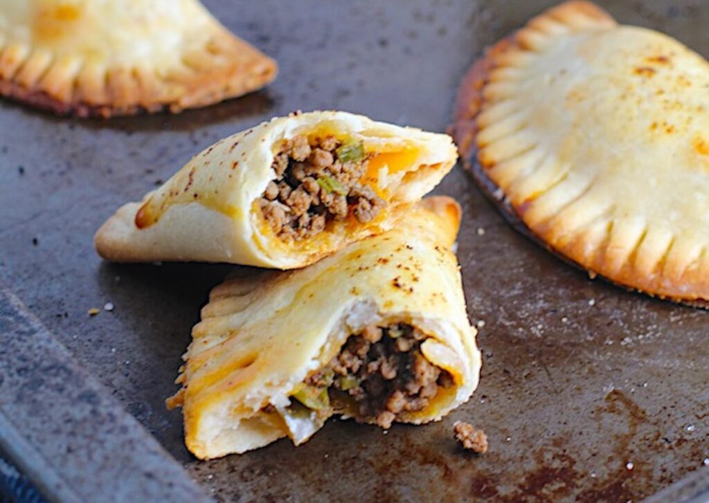 Taco meat recipe in empanadas on a sheet pan with one cut in half and stacked.