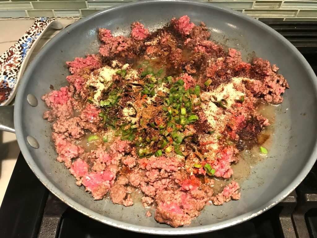 Raw ground beef in a skillet cooking with sliced scallions, Smoked paprika, cumin, chili powder, garlic powder, salt for Taco Meat Recipe.