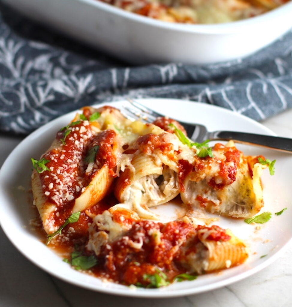 Easy Ricotta Filling recipe mixed with shredded turkey and stuffed into Pasta shells on a plate with sauce.