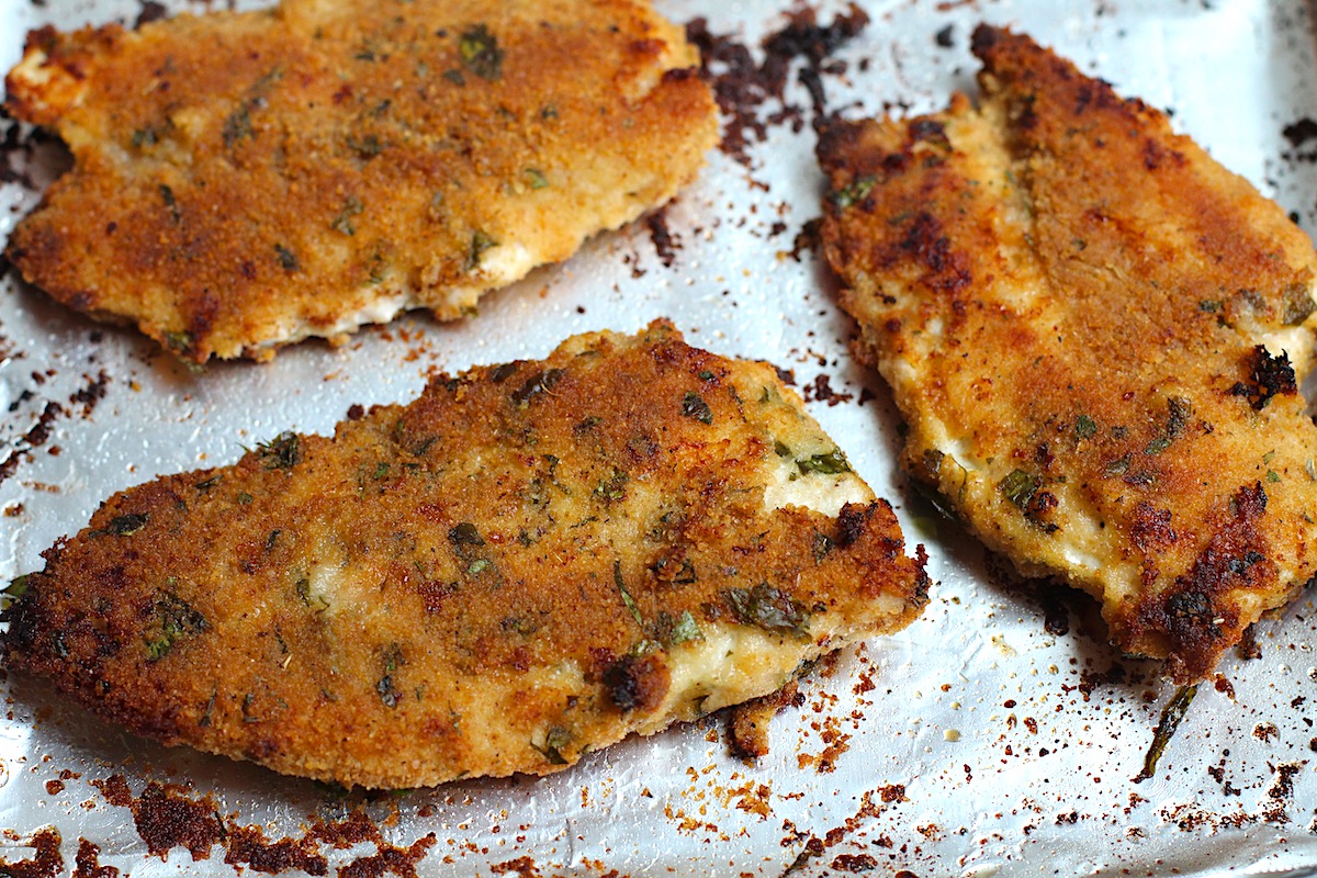 Three golden brown, baked Italian Chicken Cutlets on a sheet pan lined with aluminum foil.