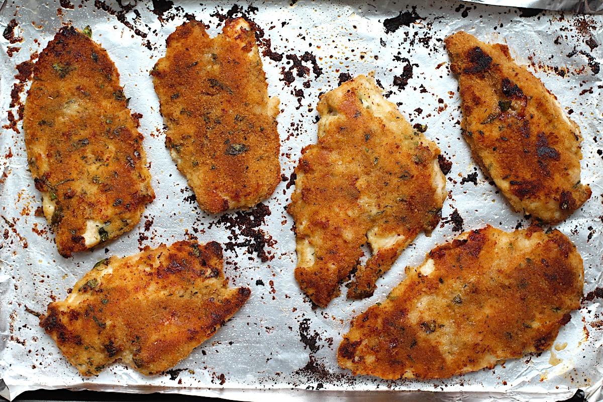 Six golden brown, baked Italian Chicken Cutlets on a sheet pan lined with aluminum foil.