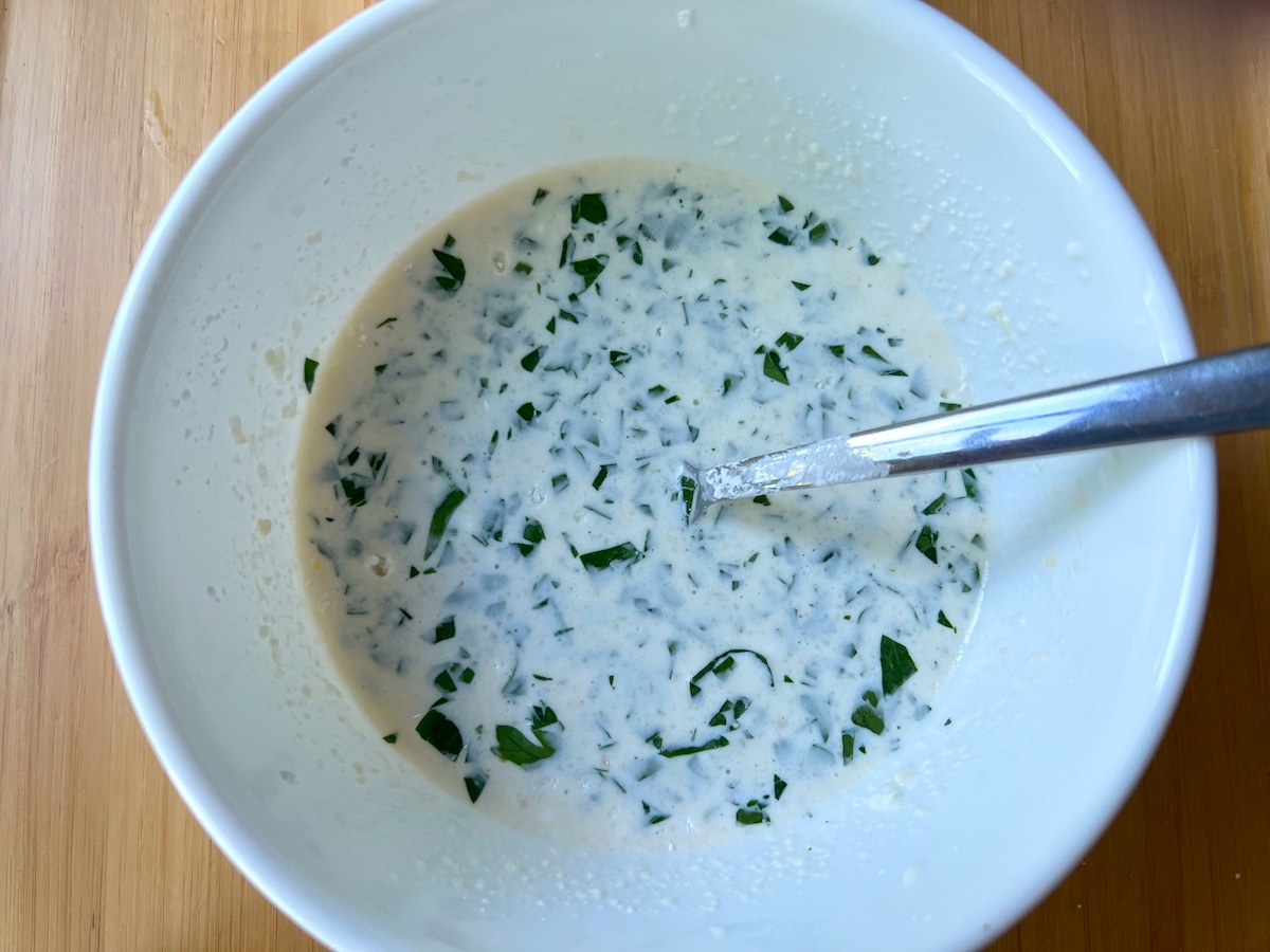 Sauce mixture in a bowl with spoon (mayonnaise, milk, parmesan, cornstarch, parsley) for White Sauce Chicken Pasta recipe.