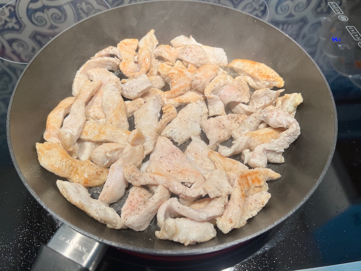 Chicken breast strips browned and cooking in a pan for White Sauce Chicken Pasta recipe.