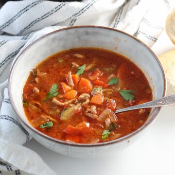 Ground Beef Vegetable Soup Recipe in a bowl with spoon on counter with blue and white towel around. It's a perfect fall meal that's comforting, hearty, and delicious with loads of veggies! Make it in the slow cooker or on the stove.