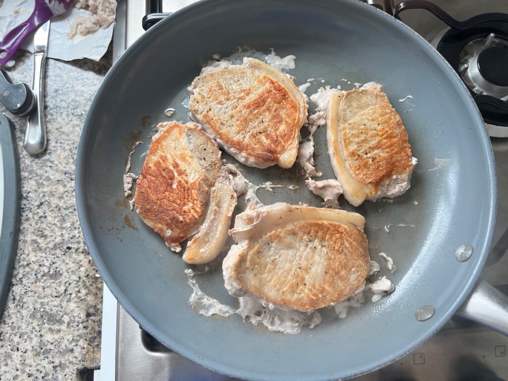 Four browned pork chops in a skillet for Pork Normandy recipe.