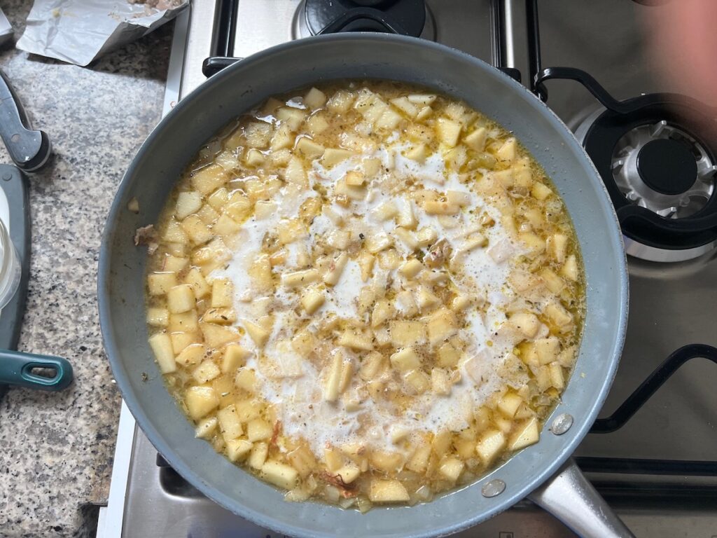 Cream and broth added to apples and onions cooking in a pan for Pork Normandy recipe.