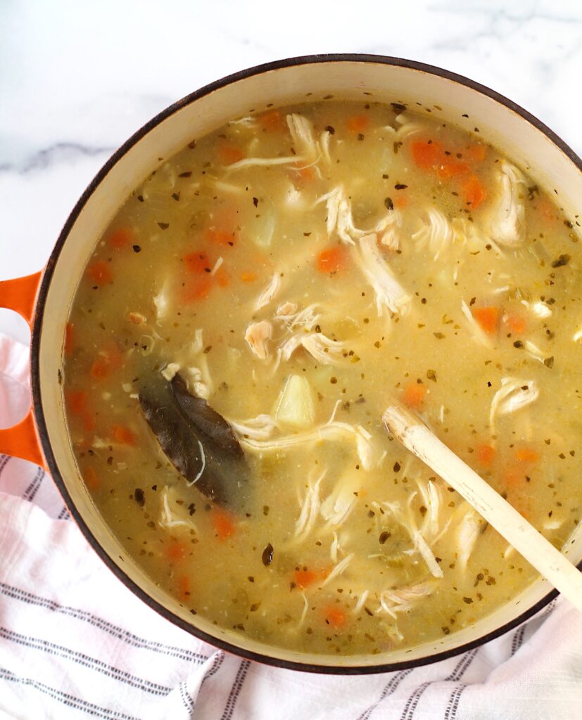 Creamy Chicken Potato Soup Recipe with carrots and celery in a dutch oven with a wood spoon on counter with towel. It's comforting, hearty, and delicious.  It's a great dinner for busy families!