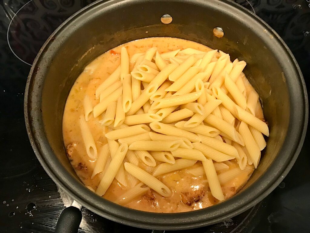 Penne Pasta added to creamy sauce in pot for Chipotle Chicken Pasta Recipe.