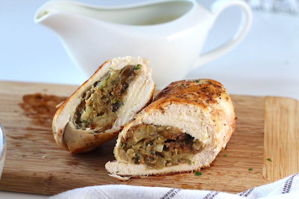 Stuffed chicken sliced in half on a cutting board with gravy boat behind it. Stuffing stuffed chicken breast recipes are easy and delicious!