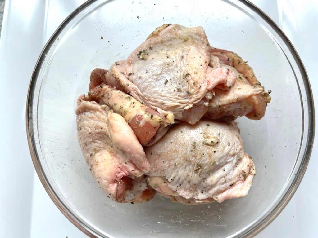 Seasoned raw chicken thighs in a bowl for Roasted chicken rice.