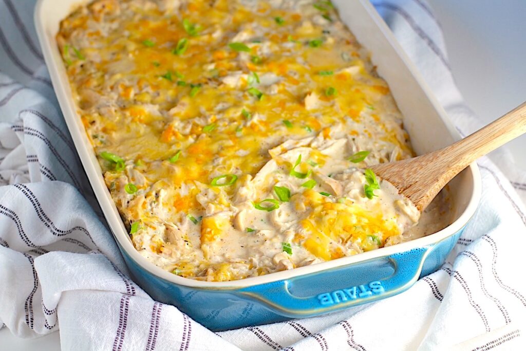 Chicken Hashbrown Casserole Recipe in a casserole dish on a towel with wooden spatula in it.