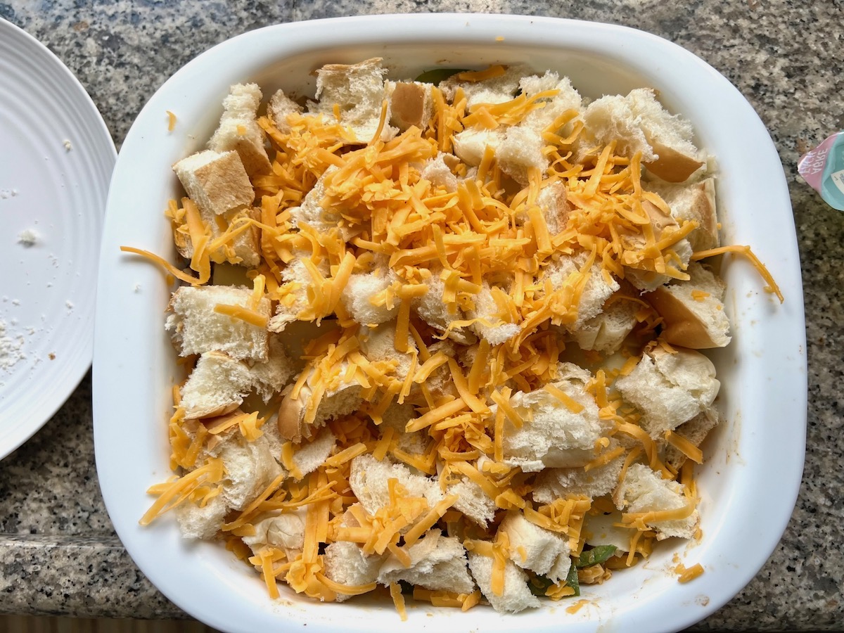 Torn bread pieces and shredded cheddar on top of Philly Cheesesteak casserole recipe with Steak before baking.