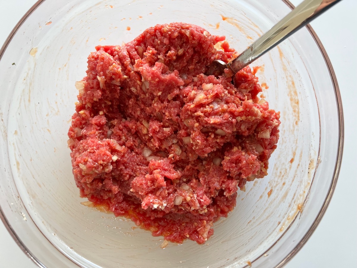Raw ground beef, diced onion, ketchup, egg, and parmesan mixed in bowl for Meatloaf Casserole Recipe.